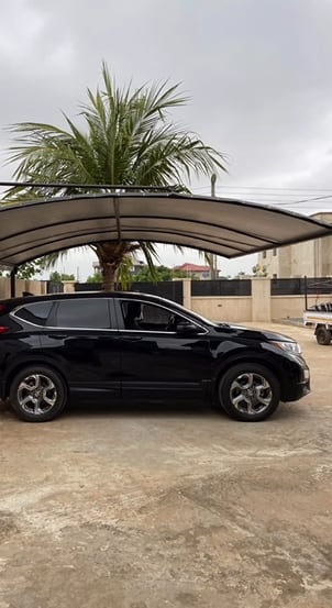 A single curved bronze polycarbonate carport over a black SUV on a residential compound